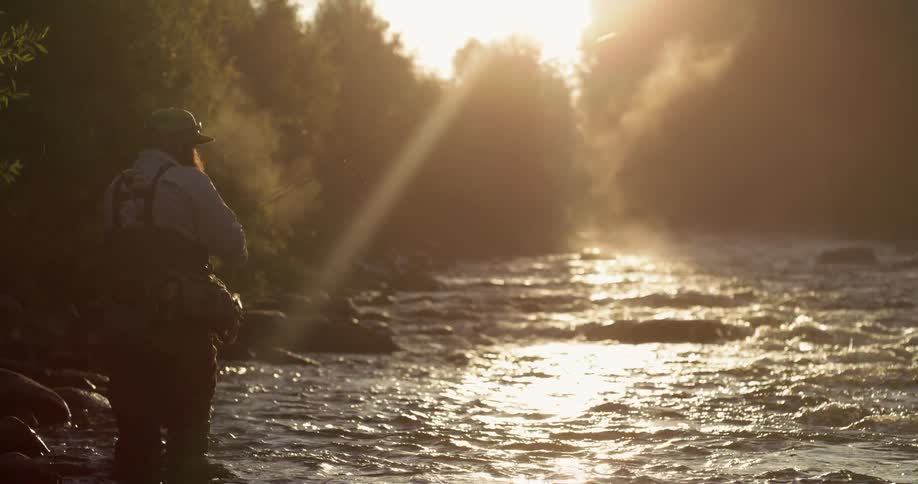 A man is wading in the waters of a stream fishing