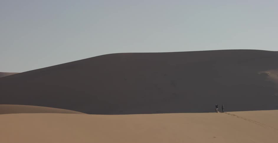 Two people are walking amid sand dunes