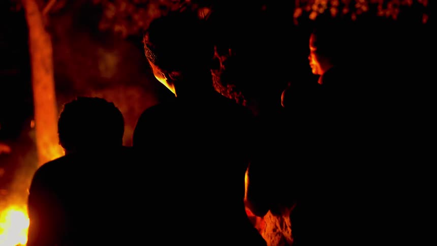 Tribe members sing and clap in front of a bonfire