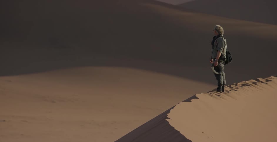 A man stands on a sand dune on a windy day