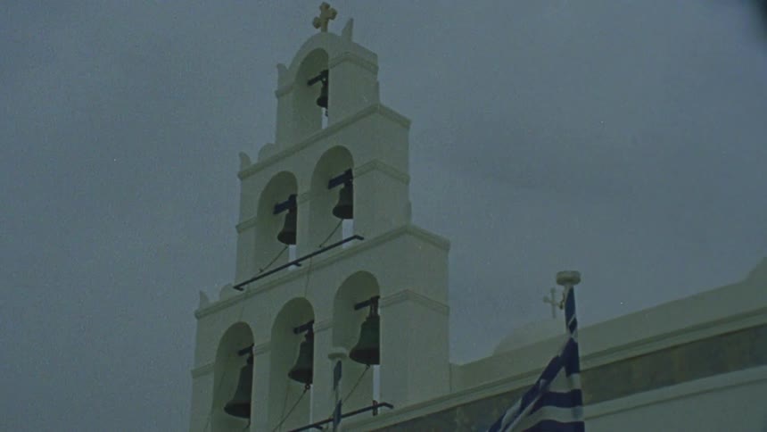 A flag flows in the breeze in front of a building with bells