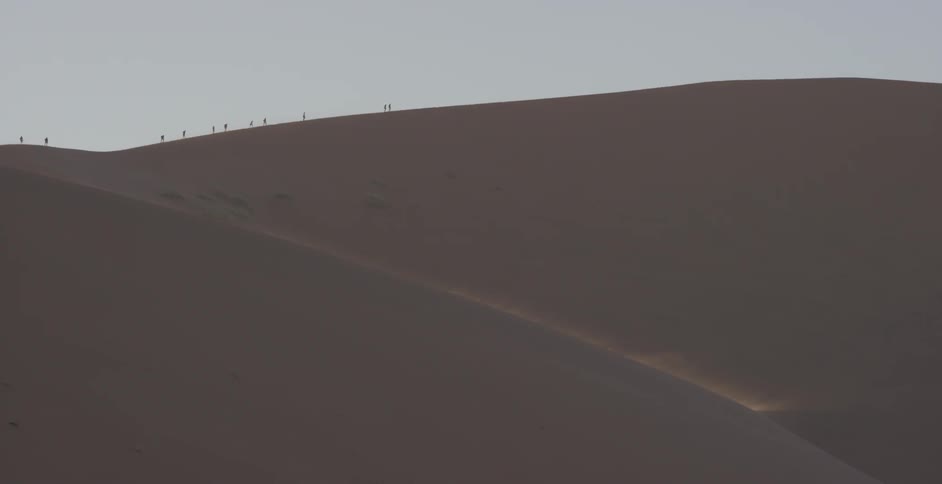 A group of people are walking on top of a sand dune