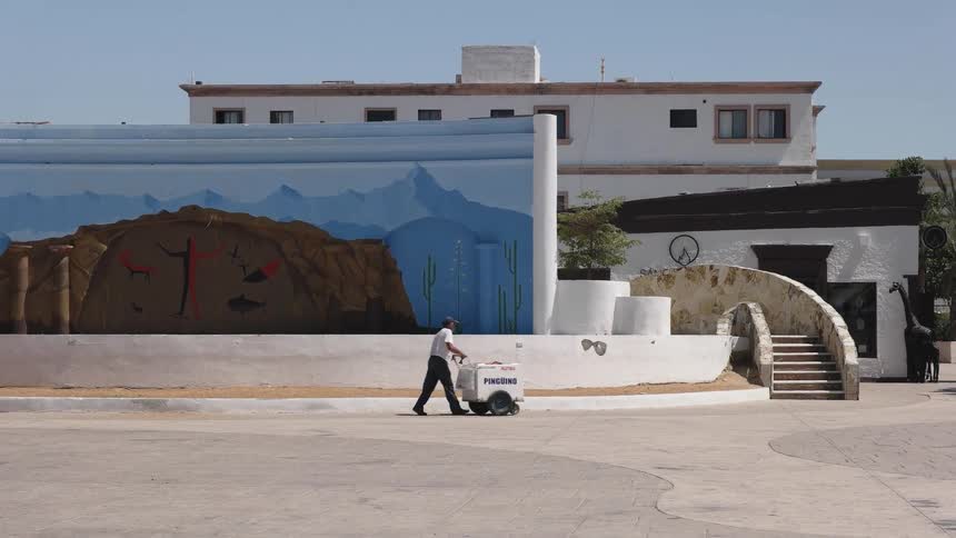 A man pushes a cart outside a building on a sunny day
