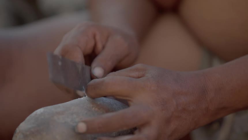 A man uses a knife to chop on a large rock
