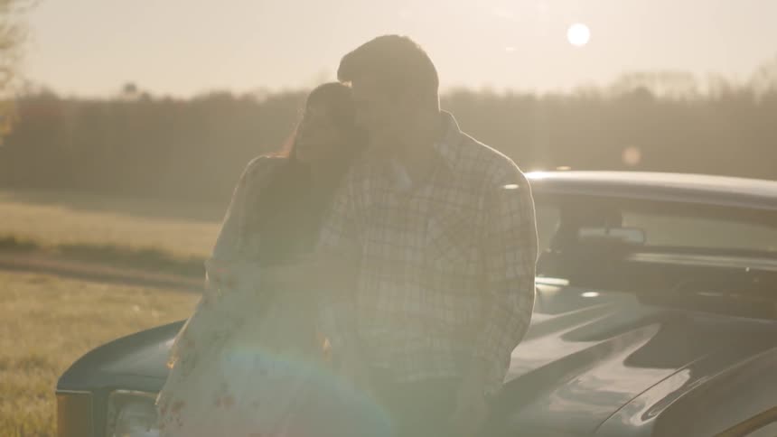 A man and woman embrace on the hood of a car