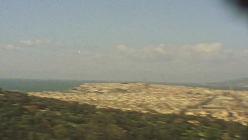 A green hill overlooks a city below