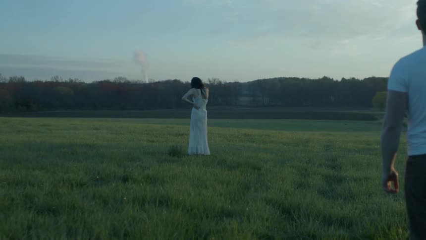 A woman stands in front of a man on a field
