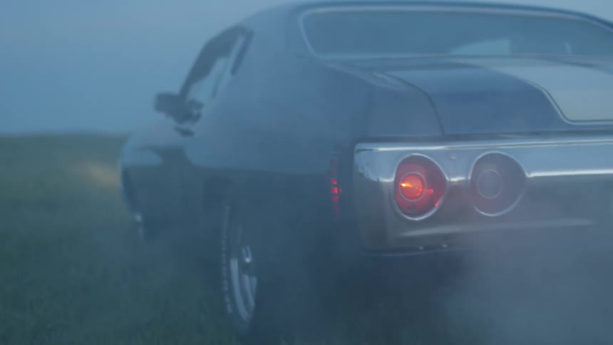 Smoke billows from the exhaust of an old muscle car