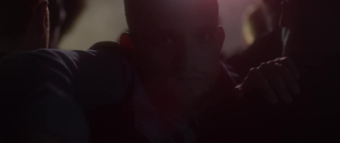 A man leans over others blocking his way as lights flash in a room