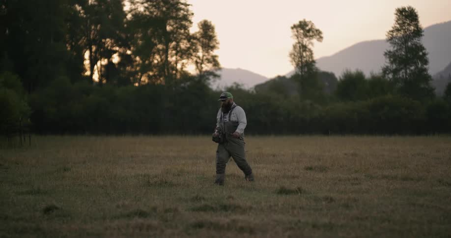 A man walks across a field holding fishing equipment