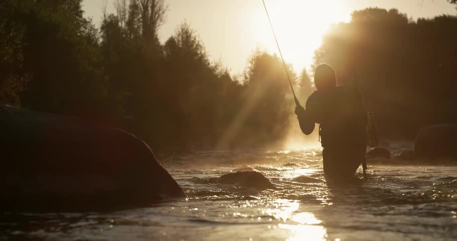 Man fly fishing in river as sun rises