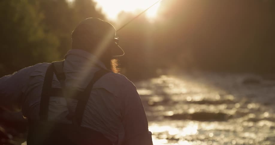 A man is fly fishing as the sun sets