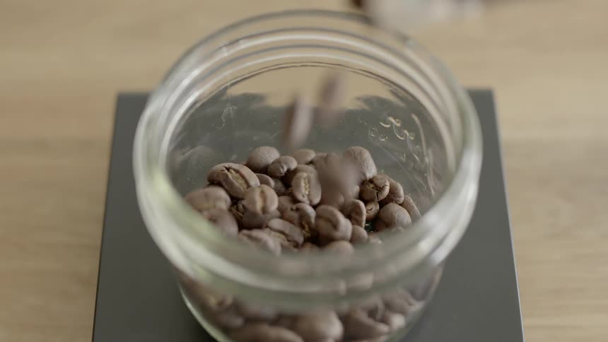 Coffee beans being poured into a glass jar