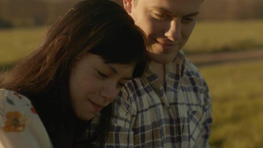 A man and woman cuddle in a rural field at sunset