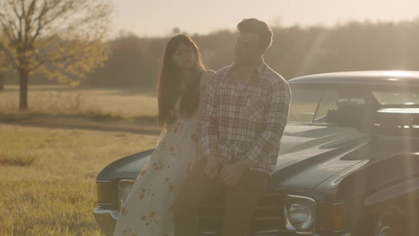 A man and woman sit on the hood of a car