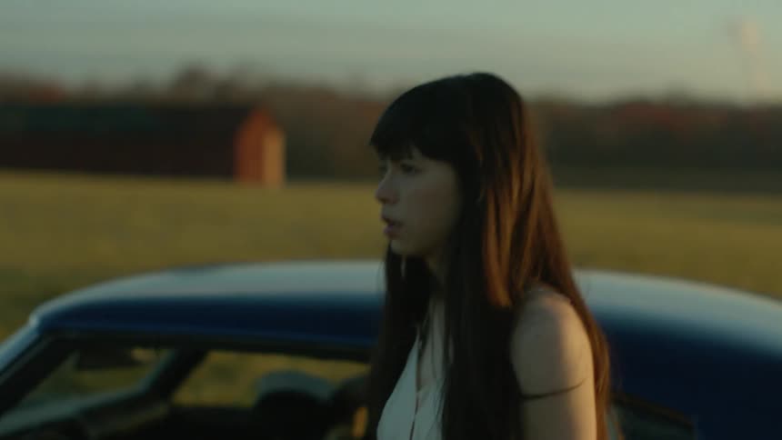 A woman walks away from a car parked in a field