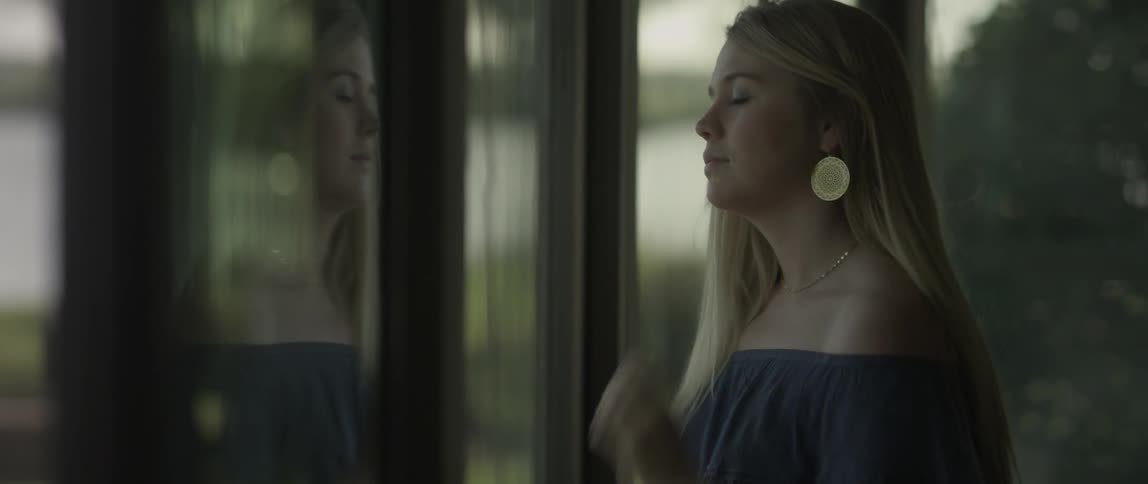 A woman adjusts her hair by the window