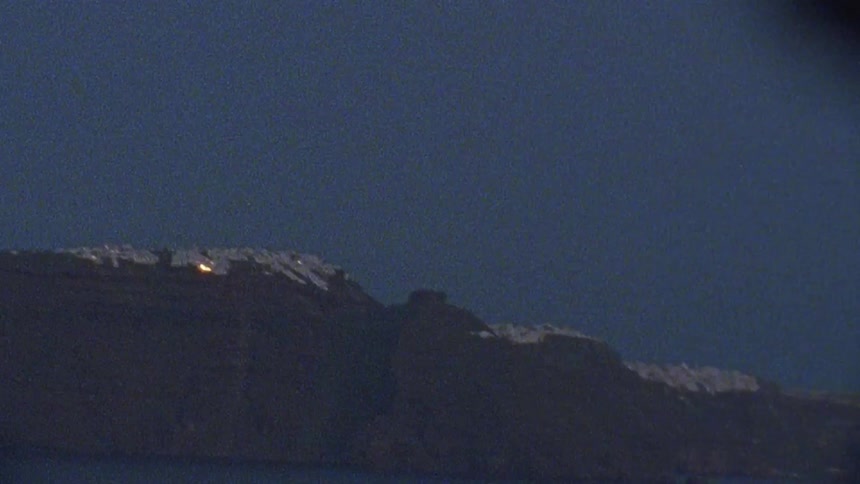 A light illuminates from a town on a shoreline hill