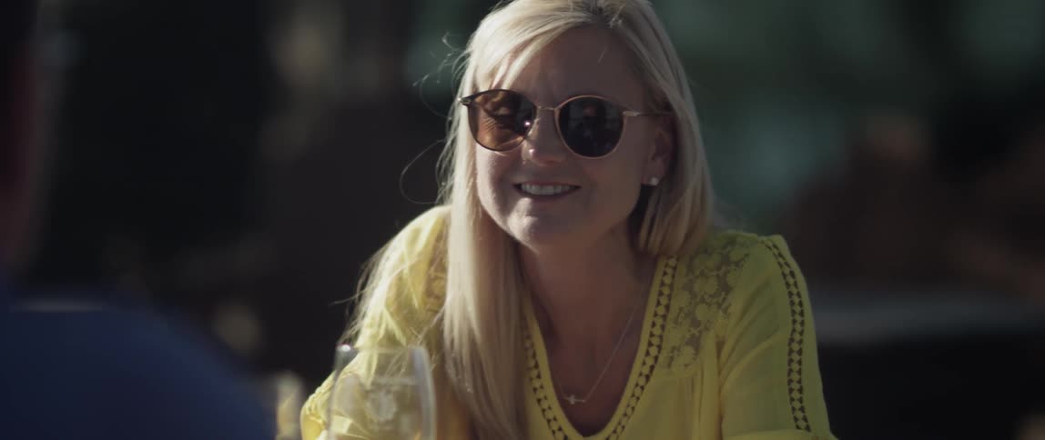 A woman is nodding and talking as she sits at a table outside