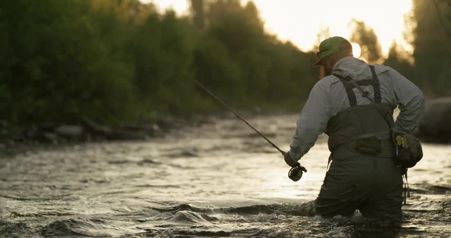 A man wades through water carrying a fishing rod
