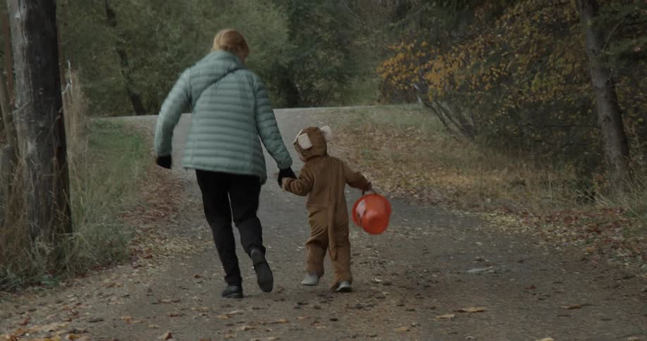 Woman holds hands with a child in a costume as they run down a path