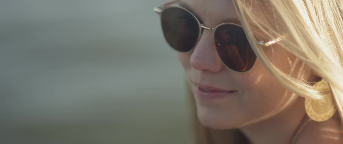 A woman wearing sunglasses smiles by water
