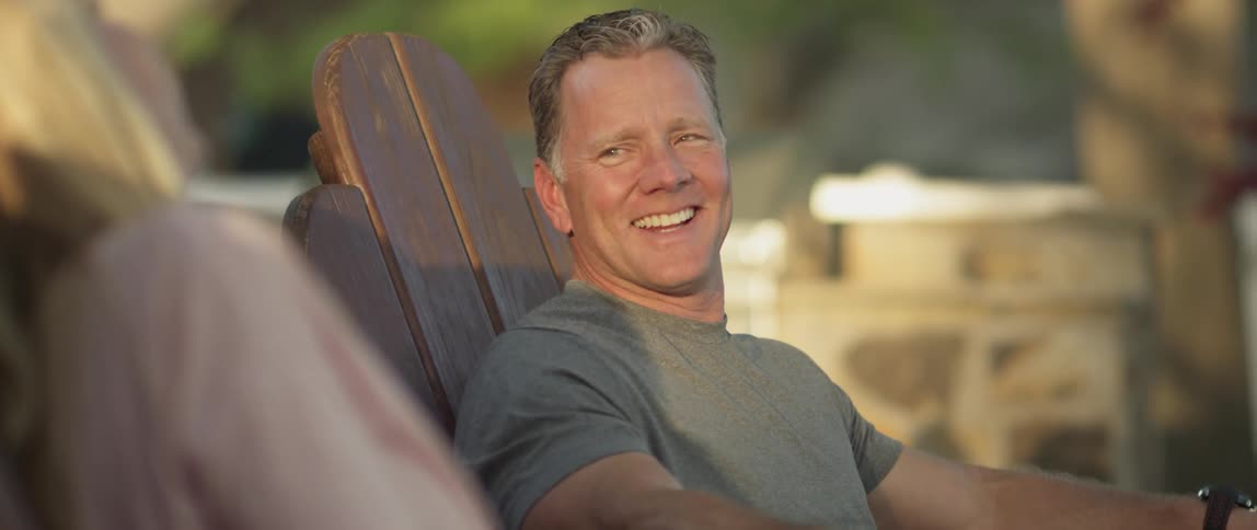 A man sitting in a chair outside smiles and laughs