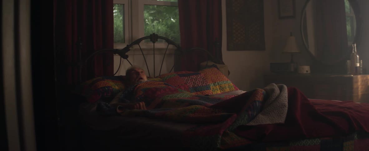 An elderly man lays in bed with a quilt