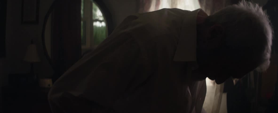 An elderly man buttons up the shirt