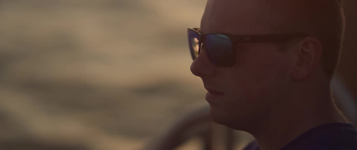 A man sits by the water wearing sunglasses