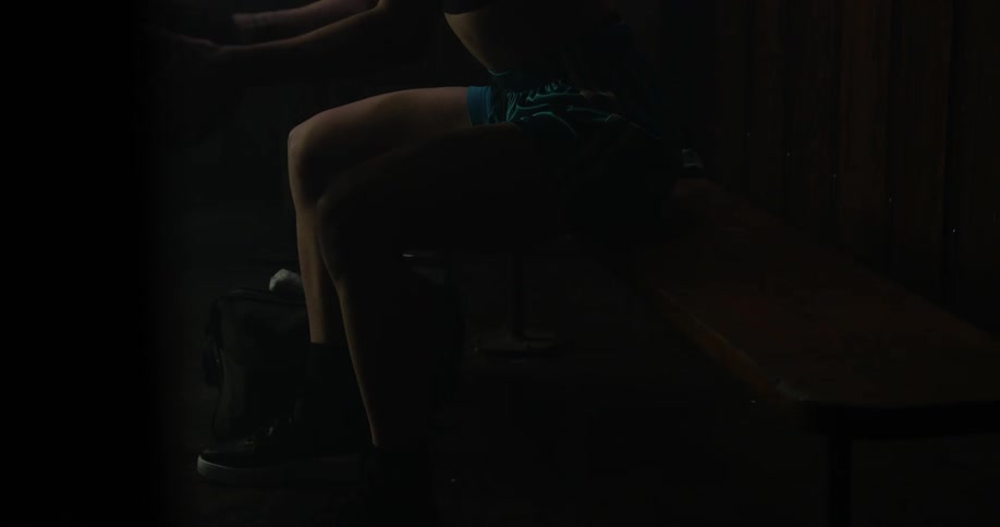 A woman sits on a bench bouncing a basketball