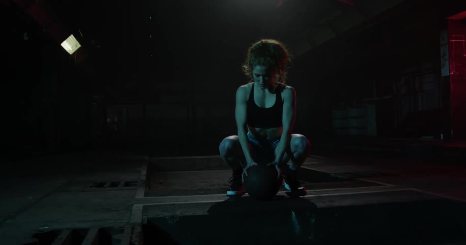 A woman squats down with her hands on a basketball