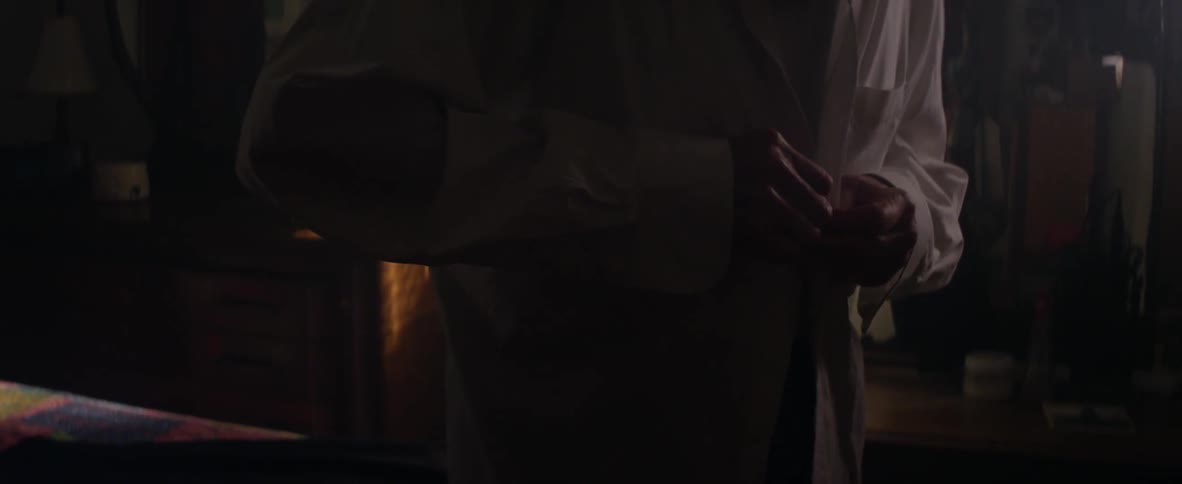 An elderly man tries to button up his shirt