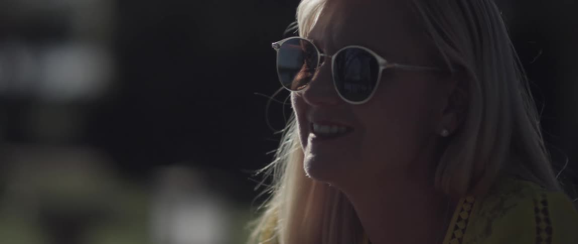 A woman smiles and talks outdoors on a sunny day
