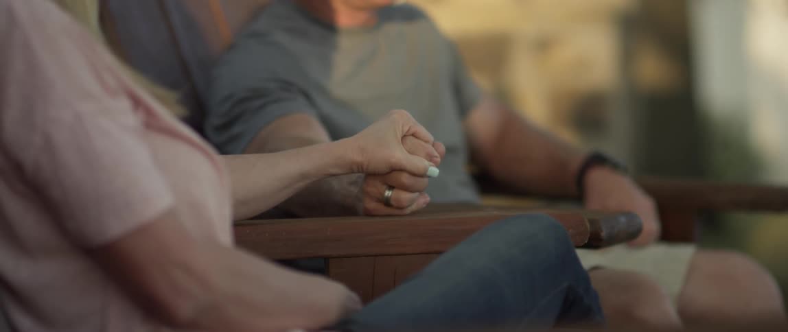 A man and woman are sitting outside holding hands