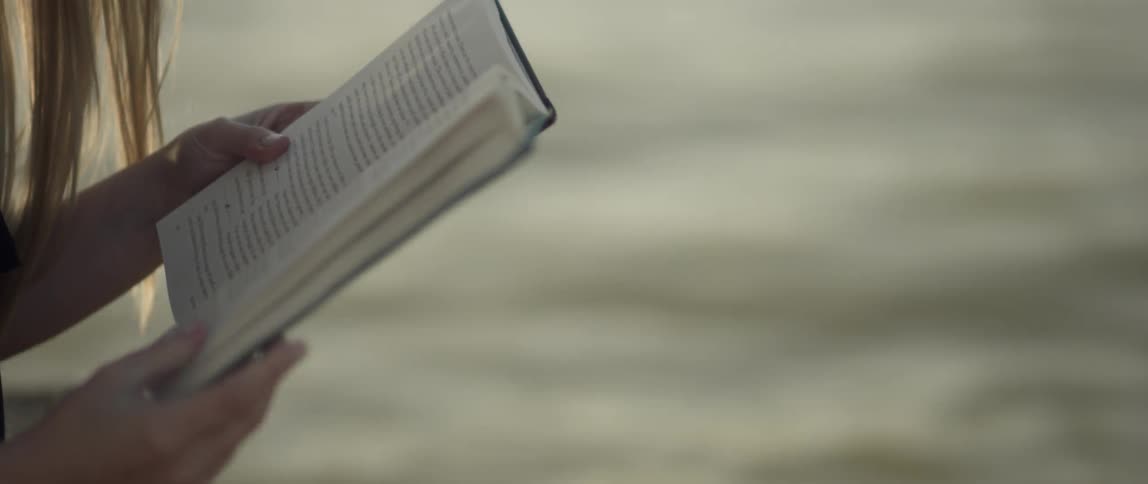 A woman reads a book outside by the water