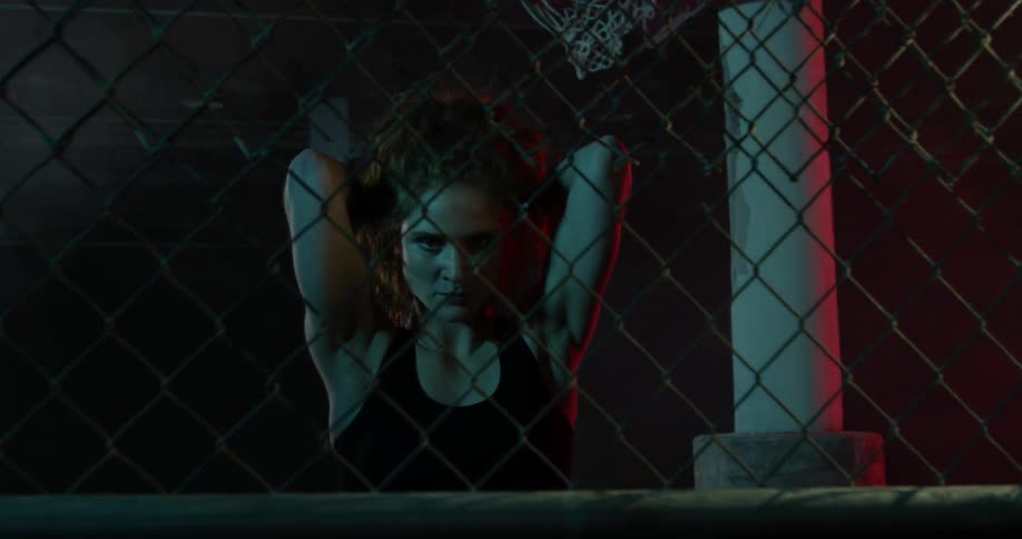 Woman stands behind fence with hands above her head