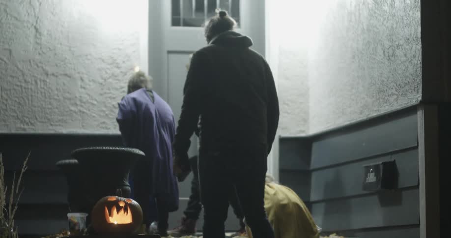 A parent walks young children to a front door to trick or treat