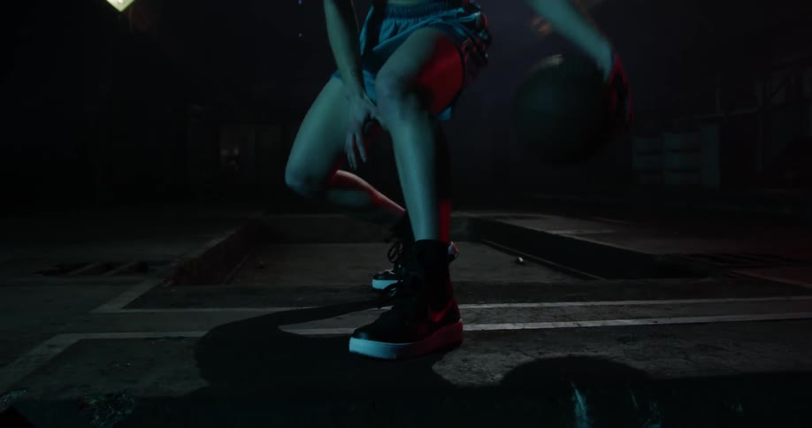 A person is bouncing a basketball fast in a dark room