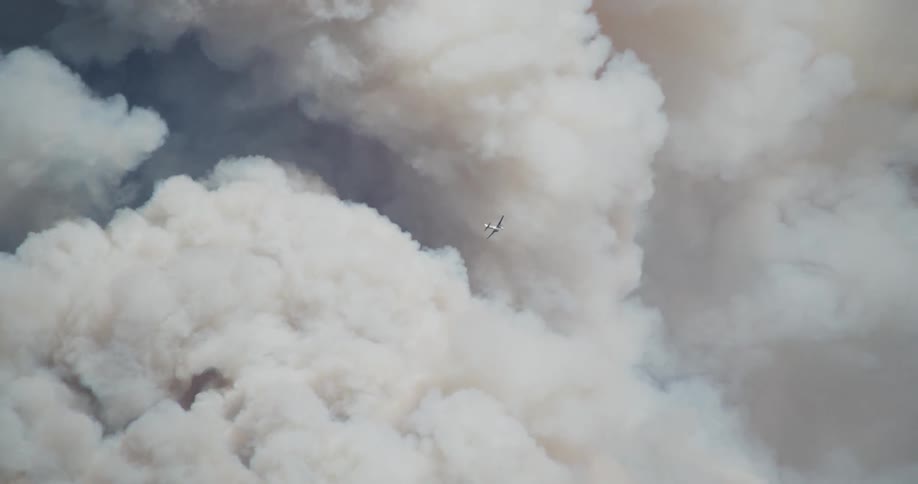 A plane flies into pluming smoke from a fire