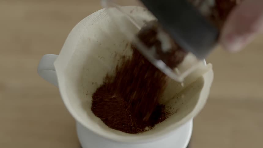 A white person sprinkles ground coffee into a filter sitting in a cup