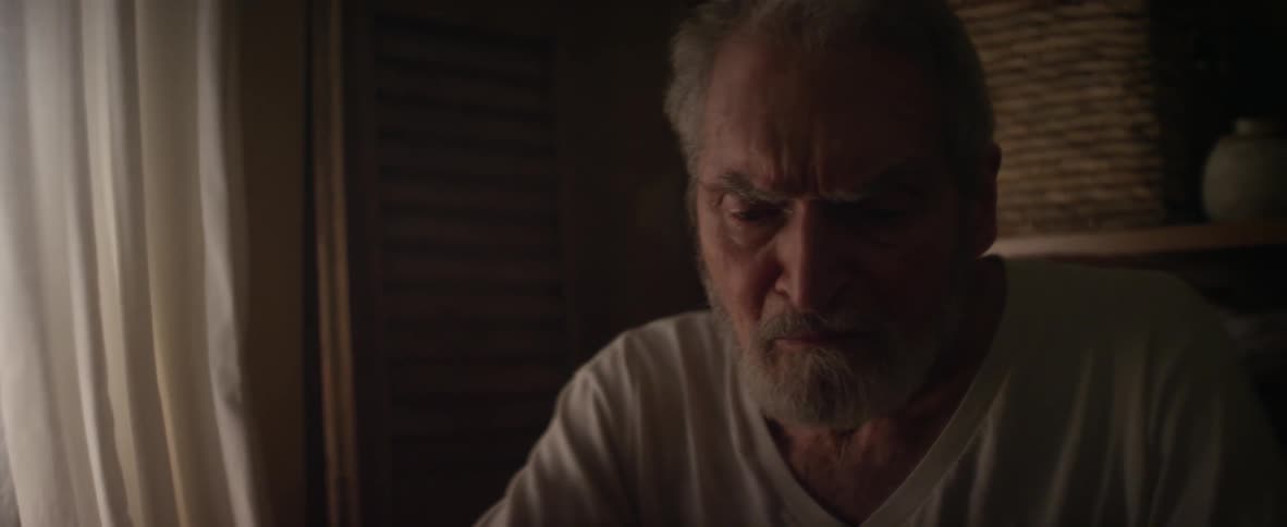 An elderly man sits and looks sad in a room