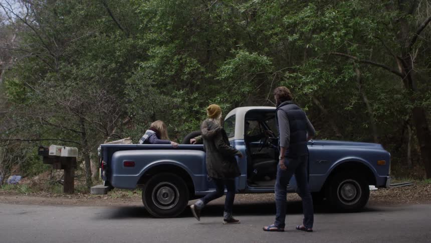Men and women get into the bed and cab of an old chevrolet pickup truck