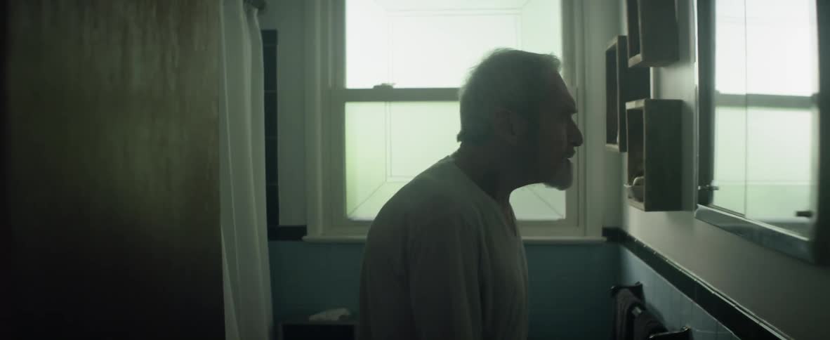 An elderly man standing in a bathroom is talking to himself