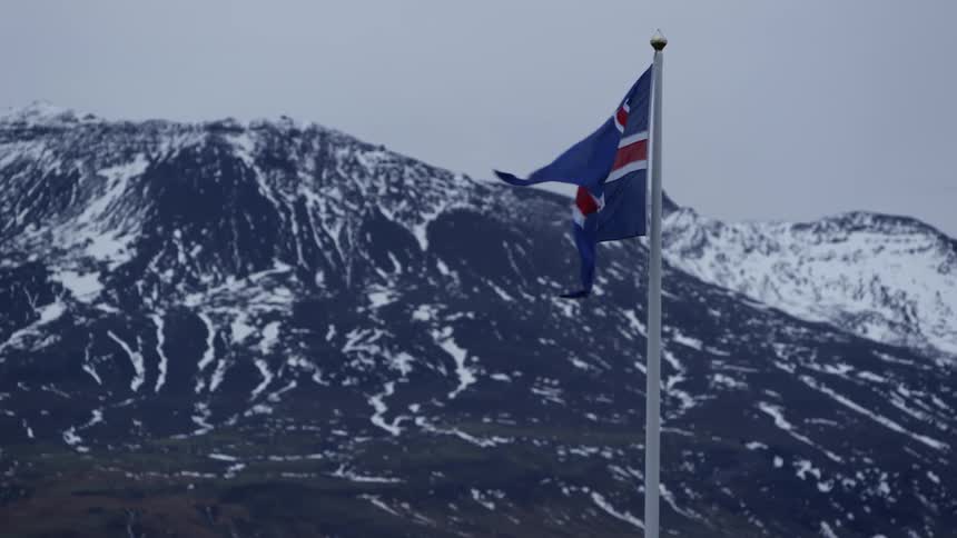 A flag billowing in the wind in front of snow-covered mountains
