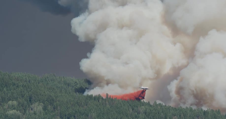 A plane drops red fire retardant on a smoking forest fire