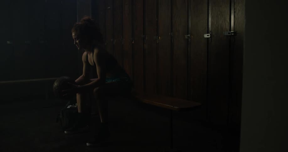 A lady is sitting in a locker room with a basketball