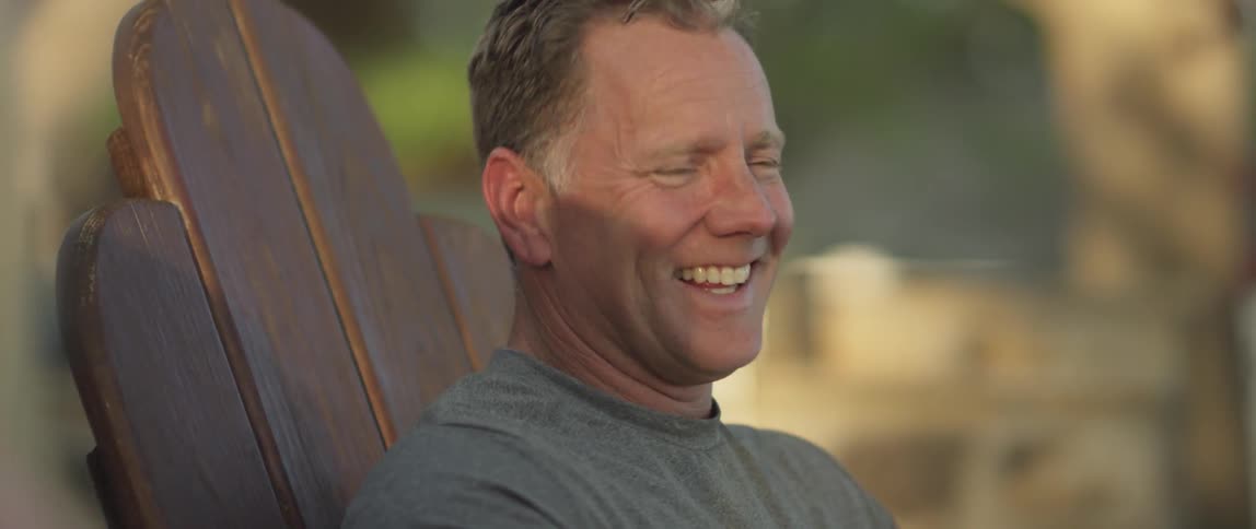 A man sits in a chair outdoors smiling