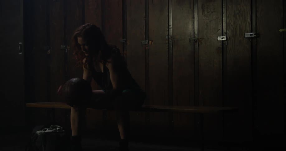 Woman sitting in dark locker room holding basketball