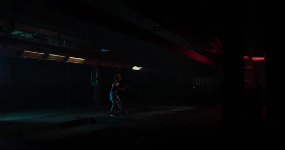 A woman bounces a basketball in a dimly lit gym